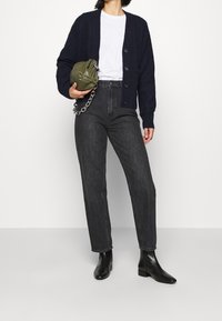 Marineblauwe wollen cardigan met knopen, wit T-shirt, high-waisted zwarte jeans, groene tas met ketting en zwarte enkellaarsjes.