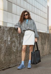 Czarna i biała koszula w paski oversize, biała spódnica, niebieskie trampki, jasnoniebieskie skarpetki i czarna torba na ramię. Gładkie tekstury, casualowy design.