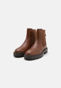 Bocanci ankle din piele maro cu panouri laterale elastice, vârf rotund și talpă din cauciuc texturat. Design minimalist, textură netedă.