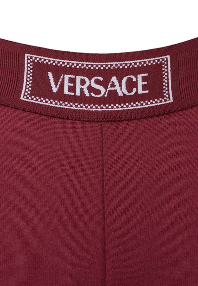 Primo piano di un tessuto a maglia marrone con una cintura a coste che presenta il testo bianco "VERSACE" e un bordo decorativo.