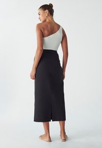 Top côtelé asymétrique en gris clair, associé à une jupe noire longueur cheville avec une fente dans le dos, portée avec des sandales plates.