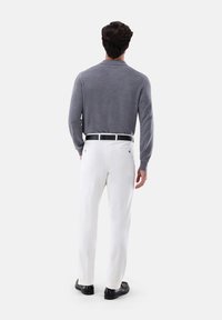Grau gestrickter Pullover mit Kragen, kombiniert mit weißen Hosen und schwarzen Schuhen. Der Stoff wirkt glatt und hat eine figurbetonte Silhouette.