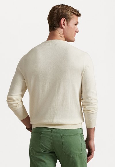 Lichtcrème trui met een ronde halslijn en lange mouwen, voorzien van geribbelde manchetten en onderrand, gedragen met groene broek. Soepele structuur.