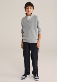 Svetlý sivý rebrovaný pletený sveter s golierom na zips, skombinovaný s čiernymi nohavicami a čierno-sivými teniskami. Jednoduchý, pohodlný dizajn bez viditeľných vzorov.