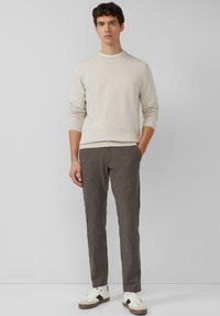 Hellbeiger Pullover mit gerippter Struktur und Rundhalsausschnitt. Graue gestreifte Hose mit konischer Passform und seitlichen Taschen. Weiße Sneaker mit beigen Akzenten.