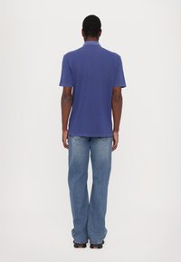 Blue polo shirt with short sleeves, paired with light blue, slightly flared denim jeans. The shirt features a classic collar and plain texture.