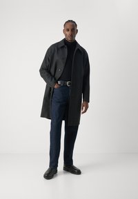 Kullgrå ullblandet frakk med rett snitt, svart høyhalset genser, mørkeblå jeans og svarte lærstøvler. Enkel knappelukking og lommer.