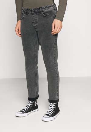 Mand iført falmede sort slim-fit jeans med op rullede manchetter og sorte høje sneakers med hvide snørebånd og såler.
