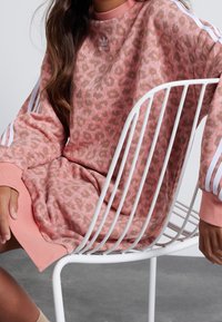 Růžová mikina s leopardím potiskem, se třemi bílými pruhy na rukávech a žebrovaným výstřihem. Materiál: bavlna.