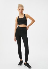 Czarny sportowy crop top i legginsy z wysokim stanem wykonane z gładkiego, elastycznego materiału, w połączeniu z czarnymi butami sportowymi.