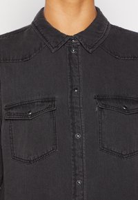 Zwarte denim overhemd met een klassieke kraag, voorzien van twee borstzakken, knoopsluitingen en subtiele stikdetails.