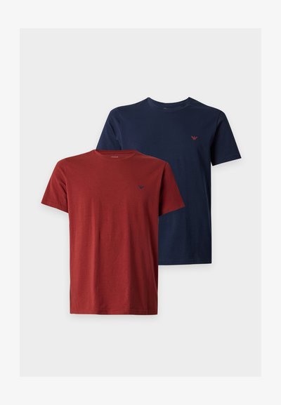 Δύο μονόχρωμα βαμβακερά T-shirts με κοντό μανίκι, ένα σε σκουροκόκκινο και ένα σε ναυτικό μπλε, το καθένα με μικρό λογότυπο στο αριστερό μέρος του στήθους.