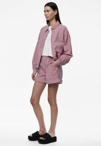 Giacca cropped a righe rosse e bianche abbinata a pantaloni corti. Presenta una vestibilità rilassata, vita elastica e sandali platform neri.