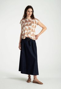 Lichtgepatroneerde blouse met korte mouwen, gecombineerd met een donkerdenim maxi rok met een strik taille en een ronde riem. Bruine platte schoenen.