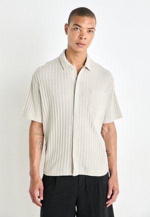 Chemise beige clair à manches courtes avec un motif côtelé texturé, patte de boutonnage, poche poitrine unique et coupe décontractée.