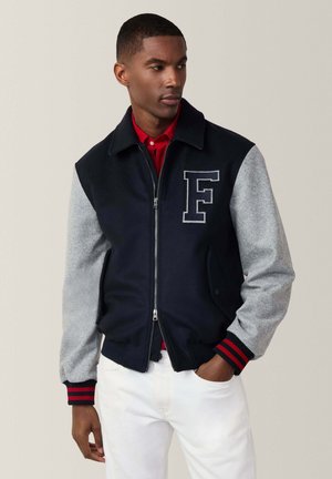 Chaqueta varsity en navy y gris con cierre frontal, cuello y puños acanalados, una gran letra "F" en el pecho y acentos en rojo a rayas.
