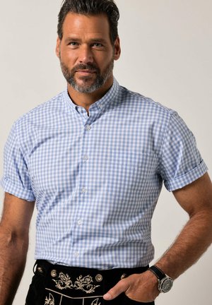 Uomo con barba e baffi che indossa una camicia a maniche corte a quadri azzurri e tradizionali lederhosen neri ricamati con orologio da polso.