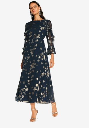 Navy blauwe jurk met rimpelige doorschijnende mouwen, versierd met gouden sterren- en maantjespatronen. Vloerlange ontwerp met een aansluitende taille.