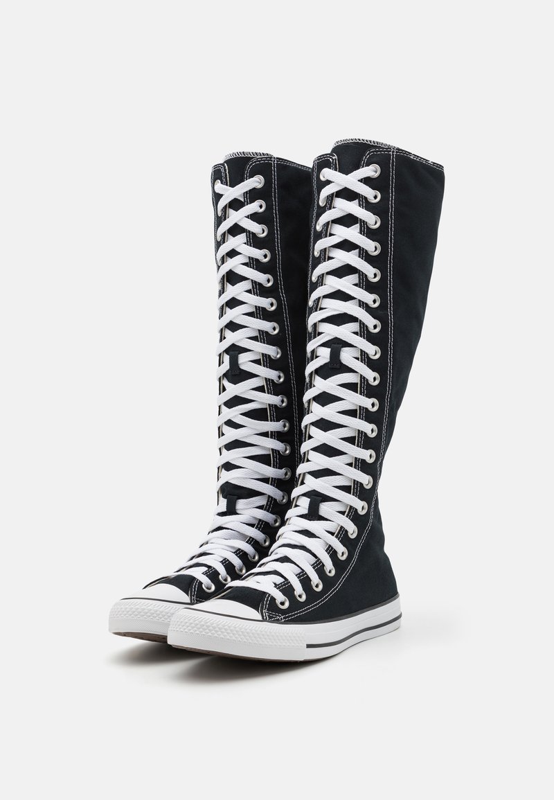 High-top black canvas sneakers with white laces, rubber soles, and contrasting white stitching along the edges. Canvas upper extends to mid-calf.