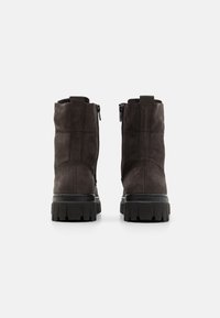 Stivaletti in suede marrone scuro con suola nera robusta. Presentano una chiusura con zip e dettagli di cucitura lungo i lati.