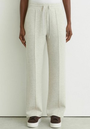 Pantalon de survêtement gris clair avec coutures devant et taille à cordon, porté par une personne se tenant devant un fond uni.