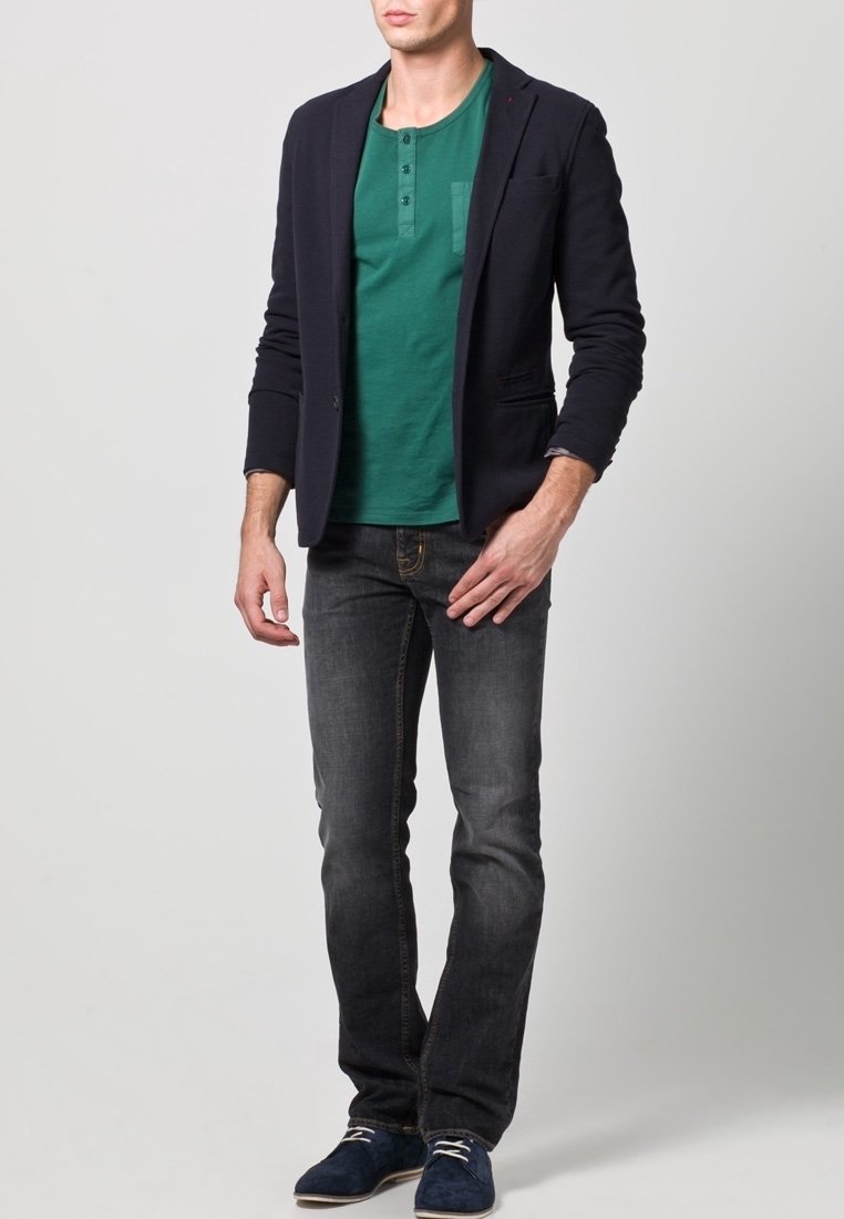 Námořnická modrá saka přes zelené henley tričko, kombinované s tmavými džínami a modrými semišovými botami. Oblečení má ležérní, ale zároveň upravený vzhled.