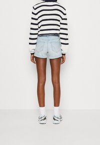 Pantalones cortos de mezclilla ligeramente desgastados con un acabado azul desvanecido, combinados con un suéter de punto a rayas blanco y negro, y zapatillas deportivas blancas.