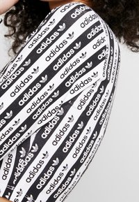 Detailní záběr na černobílý rukáv Adidas s opakujícími se logy a vzory trojlístků na látce.