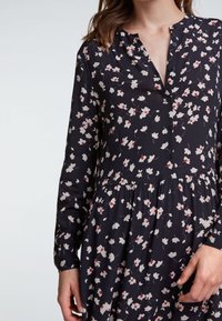 Czarna sukienka z długim rękawem z kwiatowym wzorem w bieli i czerwieni, z zapięciem na guziki i marszczonym dołem, tworzącym zwiewną sylwetkę.