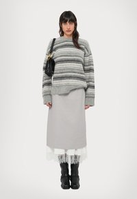 Pull rayé gris à coupe ample, jupe grise superposée, bordure en dentelle blanche, et bottes noires jusqu'aux genoux. Porte un sac à main noir avec une bandoulière en chaîne.