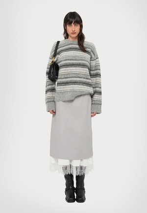 Szary sweter w paski o luźnym kroju, warstwowa szara spódnica, białe koronkowe wykończenie i czarne kozaki do kolan. Niesie czarną torebkę na łańcuszkowym pasku.