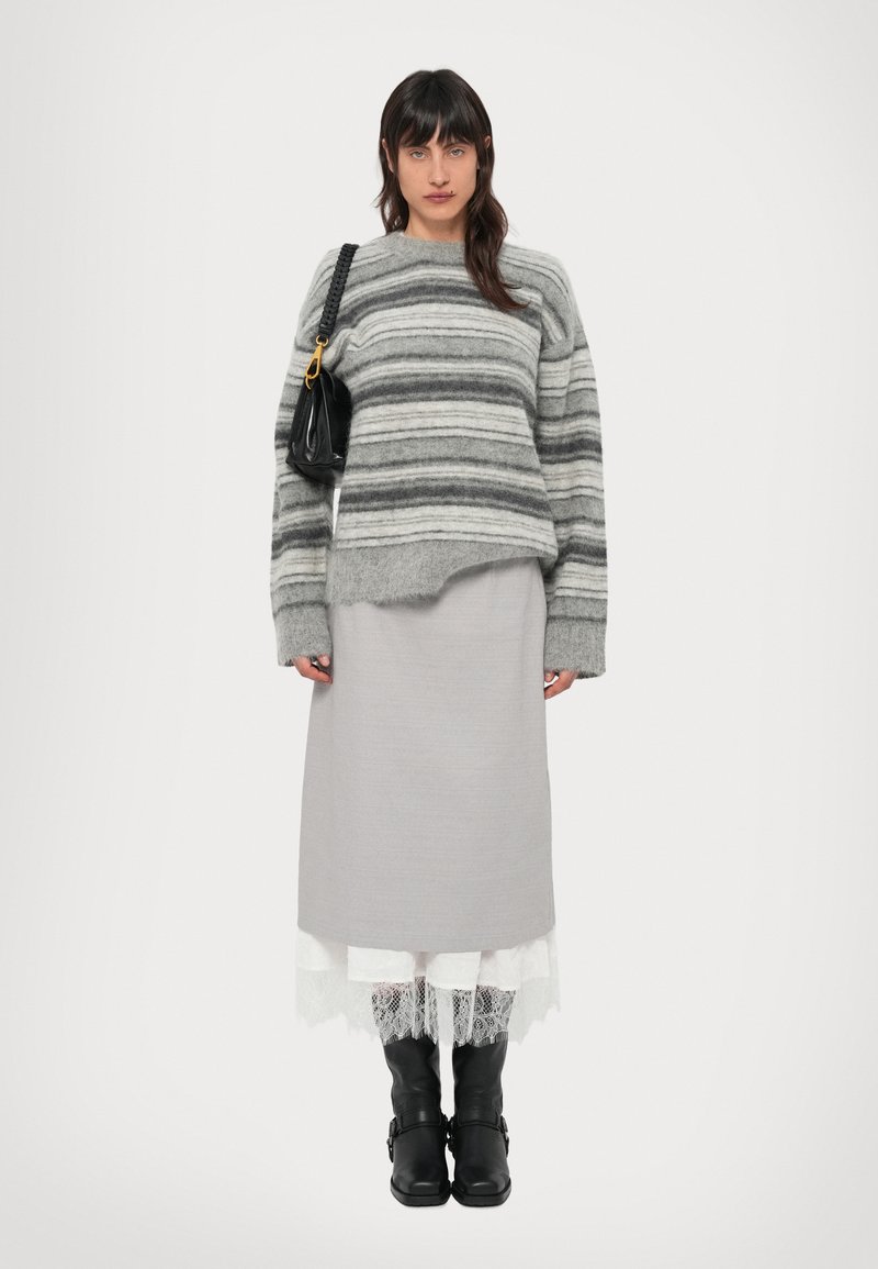 Pull rayé gris à coupe ample, jupe grise superposée, bordure en dentelle blanche, et bottes noires jusqu'aux genoux. Porte un sac à main noir avec une bandoulière en chaîne.