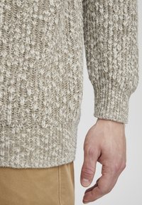 Light gray knitted sweater featuring a textured pattern with prominent white flecks, ribbed cuffs, and a relaxed fit. Handmade appearance.