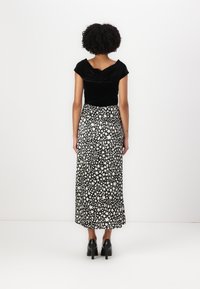 Schwarzes Samtoberteil mit rundem Rückenausschnitt; langer Rock in Schwarz-Weiß mit abstrakten Mustern; kombiniert mit schwarzen High Heels.