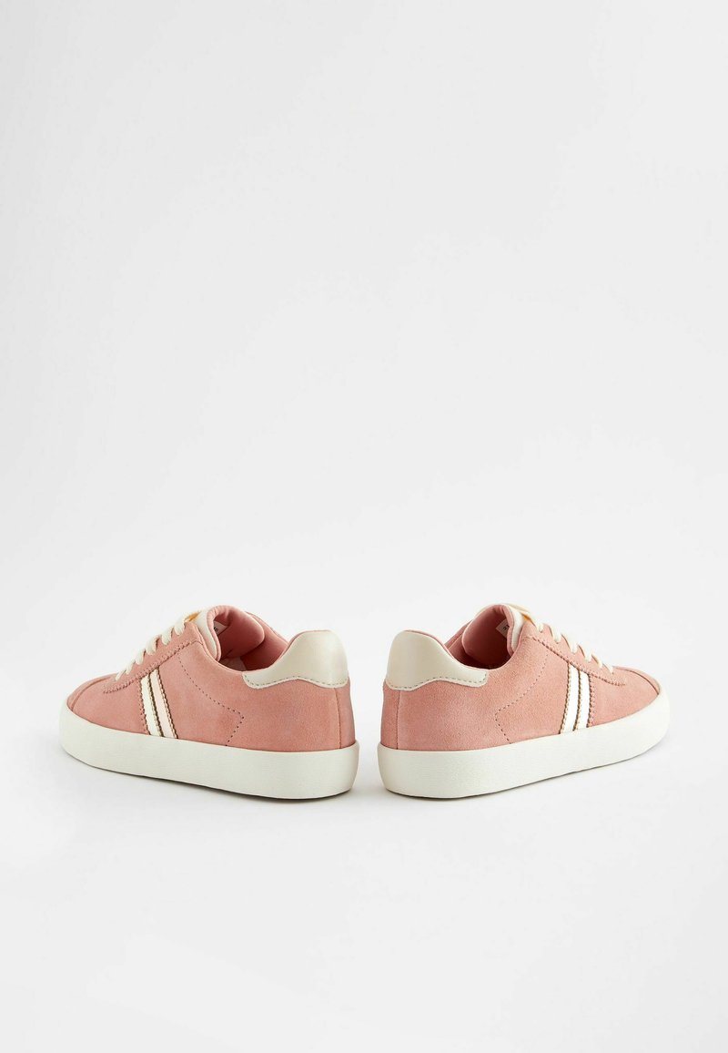 Zapatillas de ante rosa con acentos en crema y dos rayas laterales blancas. Punta redondeada y suela plana de goma con diseño de cordones.
