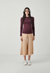 Duga mauve majica s dugim rukavima sa sakupljenim središtem i labavim bež plisiranim culottes hlačama, uparena s bijelim tenisicama i kutnim naočalama.