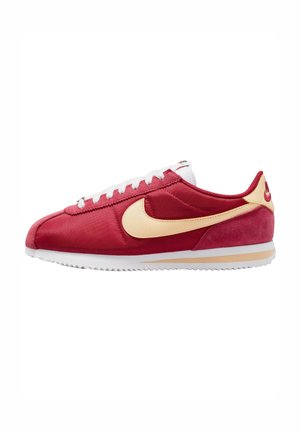 Rode en beige Nike Cortez sneaker met witte veters en zool, zijaanzicht op een witte achtergrond.