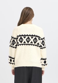 Maglione crema con motivo geometrico nero, tessuto testurizzato, maniche lunghe e polsini a coste. Vestibilità rilassata, scollo rotondo, finitura morbida.