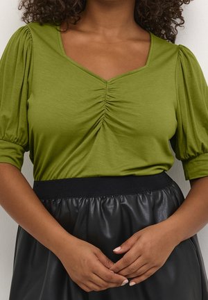 Groene V-hals blouse met geplooide details bij de borst en korte, pofmouwen, gecombineerd met een zwarte, elastische taille rok van imitatieleder.