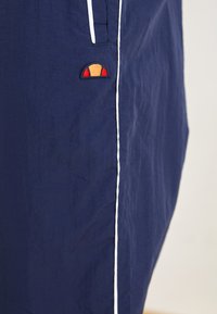 Marineblå shorts lavet af letvægtsstof med hvid kant og et lille broderet logo i rød, orange og blå farver.