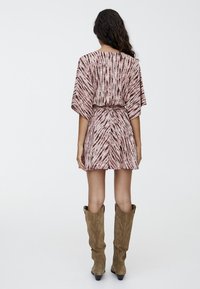 Short, pink dress with a tie-dye pattern, short sleeves, elastic waist, and a flowy silhouette. Paired with knee-high suede boots.