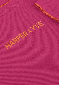 Fuchsia geribbelde stoftop met een geschulpte oranje halslijn. "HARPER & YVE" is in oranje garen aan de voorkant geborduurd.