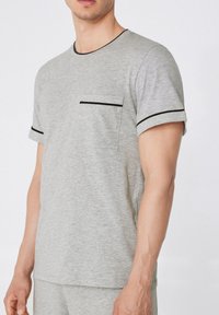 Camiseta gris de manga corta hecha de un tejido suave, con un escote redondeado, ribete negro y un bolsillo en el pecho con una franja negra contrastante.