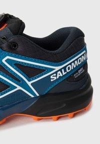 Men's trail running shoe in navy and blue, featuring a mesh upper, waterproof fabric, and orange rubber sole with traction lugs.