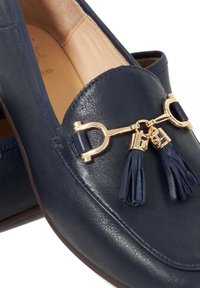 Navy leather loafers featuring a gold-tone accent with tassels, smooth texture, and rounded toe design. Brown rubber sole visible.