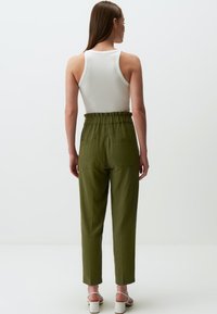 Groene, hoog uitgesneden broek met een elastische tailleband en twee achterzakken, gecombineerd met een witte, geribbelde tanktop.