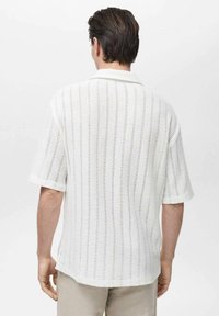 Witte shirt met korte mouwen van een textuur gebreide stof, voorzien van verticale strepen en een geribde kraag. De achterkant is eenvoudig, met subtiele details.