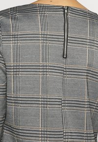 Černobílá károvaná látka se zlatými akcenty, vybavená zadním zipem a strukturovaným designem. Hladká textura s detailem mřížkového vzoru.