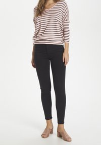 Randig rosa och svart oversized topp, kombinerad med svarta skinny jeans och ljusrosa blockklack-sandaler. Mjukt tyg med avslappnad passform.