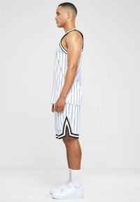 Hvid basketball tank top og shorts med sorte vertikale striber, der har en kontrasterende sort kant. Afsluttet med hvide sneakers.